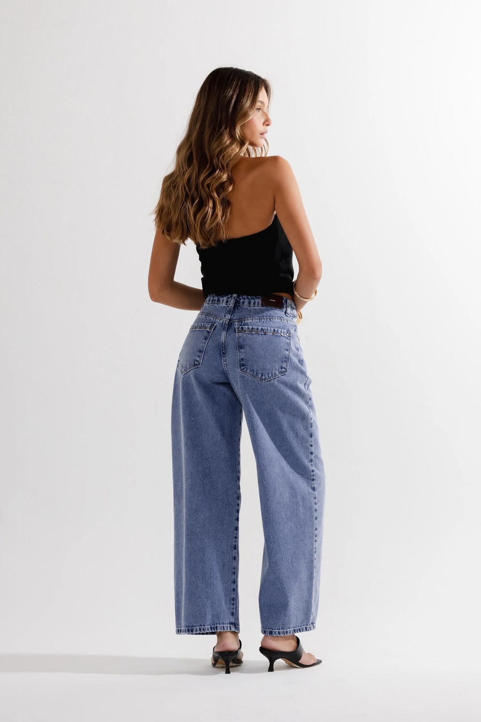 Modelo de costas usando top preto e calça jeans wide leg