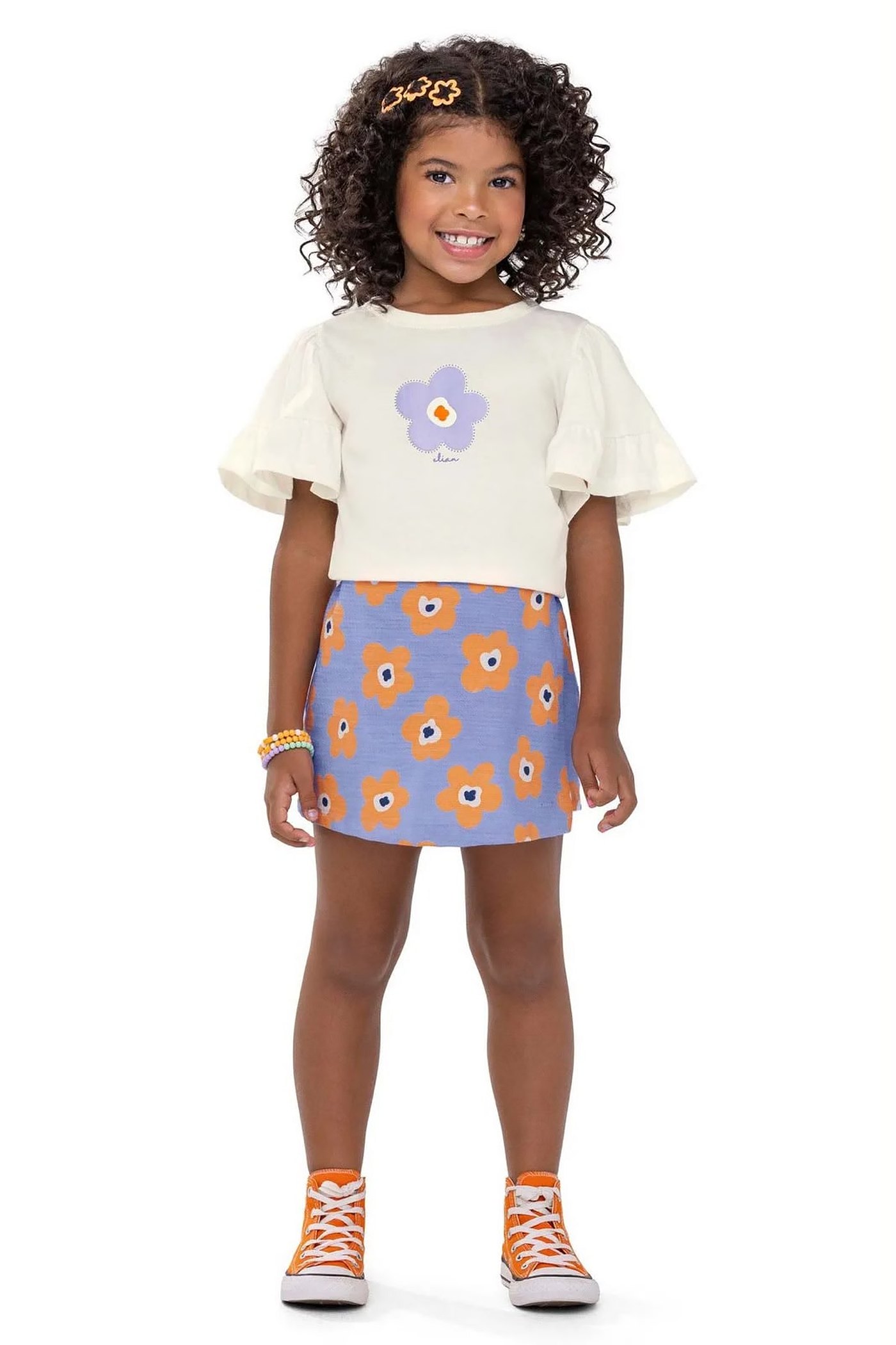 Menina usando camiseta off white com flor lilás e saia azul com flores laranja