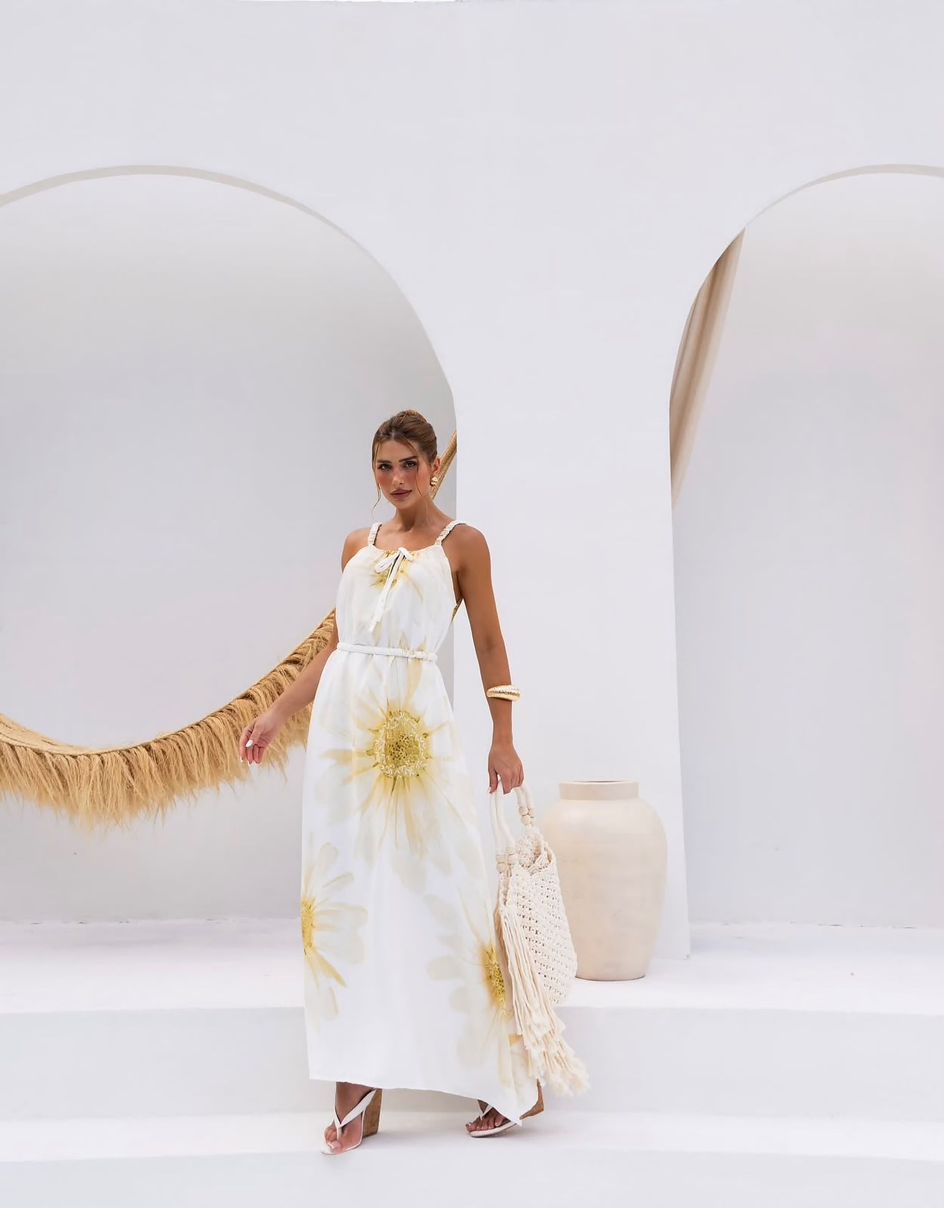 Modelo usando vestido longo branco com estampa de flores amarelas, cinto de cordão e bolsa de crochê